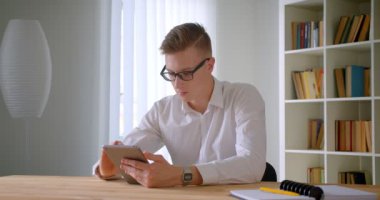 Ofiste kamera kapalı bakarak tablet kullanarak gözlük genç yakışıklı kafkas işadamıcloseup portre