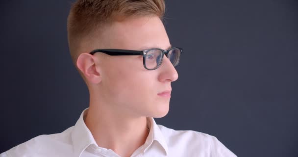 Close-up portret van jonge knappe Kaukasische man in glazen kijken naar camera met achtergrond geïsoleerd op grijs — Stockvideo