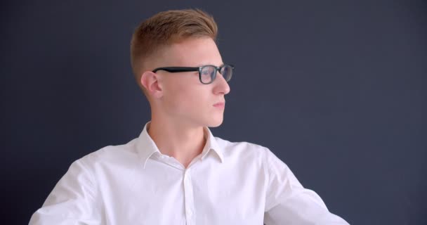 Closeup portré fiatal csinos kaukázusi üzletember a szemüveg nézi kamera háttérrel izolált szürke — Stock videók