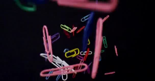 Closeup macro shoot in detail of paperclips of different colors being dropped with background isolated on black — Stock Video