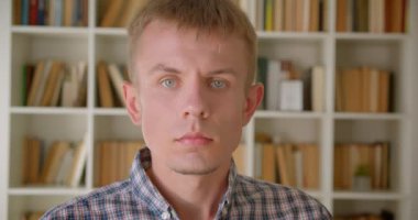 Kafkas kütüphanecisinin kitaplıklarda kameraya dikkatle ve ciddi bir şekilde izlediği portresi.