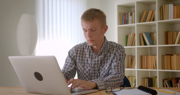 Porträt eines kaukasischen Geschäftsmannes, der aufmerksam mit Laptop auf Bücherregalen arbeitet. — Stockvideo