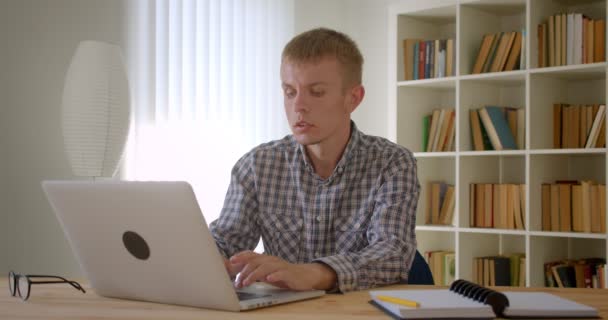 Porträt eines kaukasischen Geschäftsmannes, der aufmerksam mit Laptop arbeitet und Notizen auf Bücherregale schreibt. — Stockvideo