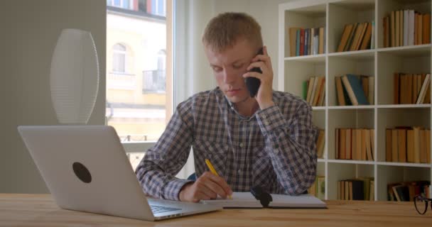 Portret van Kaukasische zakenman typen op laptop aandachtig een voicecall bezig met boekenplanken achtergrond. — Stockvideo