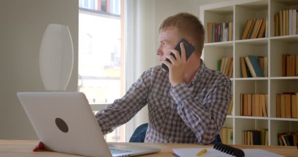 Kaukasische zakenman zittend in de voorkant van de laptop met een voicecall wordt druk en attent op boekenplanken achtergrond. — Stockvideo