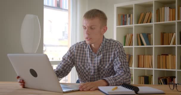 Caucásico hombre de negocios hablando en videochat utilizando el ordenador portátil en los estantes de fondo . — Vídeo de stock