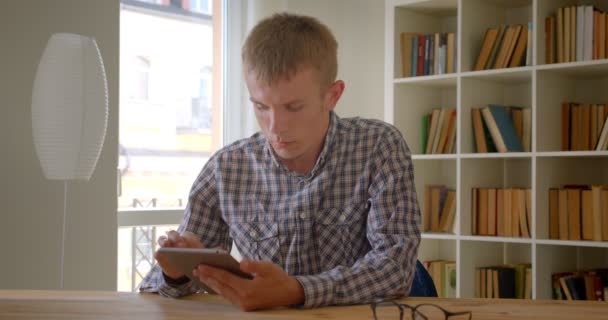 Portrait d'homme d'affaires caucasien travaillant avec tablette moderne attentivement sur fond de bibliothèque . — Video