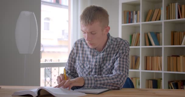 Retrato de estudante caucasiano escrevendo trabalhos de casa concentrados e atentos na biblioteca . — Vídeo de Stock
