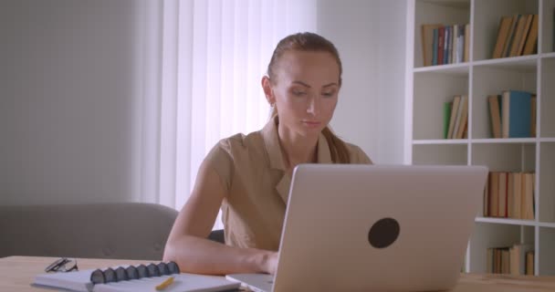 Empresária caucasiana elegante analisando dados no laptop se transforma em câmera e assiste a sério no escritório . — Vídeo de Stock