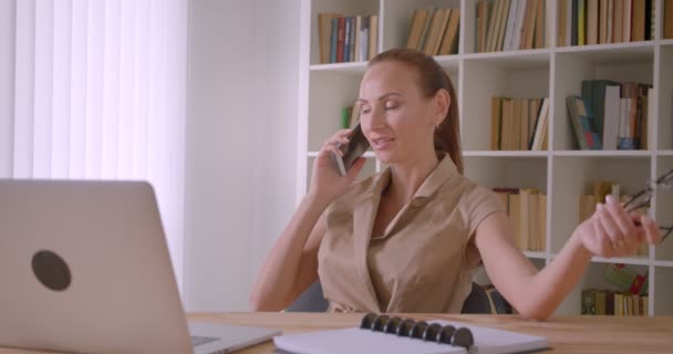 Relajada mujer de negocios delante de las conversaciones portátiles en el teléfono celular jugando con gafas en la oficina . — Vídeo de stock