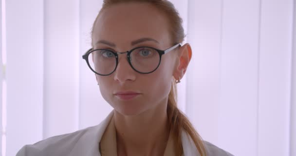 Gorgeous kaukasiska läkare i vitt päls och glasögon ler i kameran på sjukhuset på persienner bakgrund. — Stockvideo