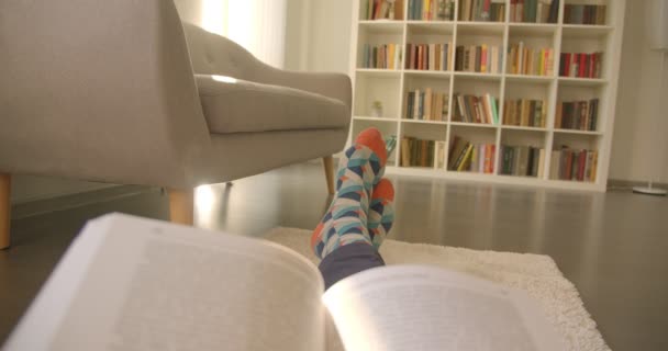 Gros plan sur les jambes des hommes assis couchés sur le sol et les mains tenant un livre détendu avec des étagères à l'arrière-plan — Video