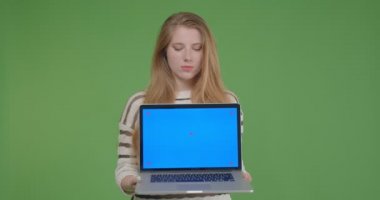 Dizüstü bilgisayarı tutan ve yeşil üzerinde izole arka plan ile kameraya mavi ekran gösteren genç güzel beyaz kadın Closeup portre