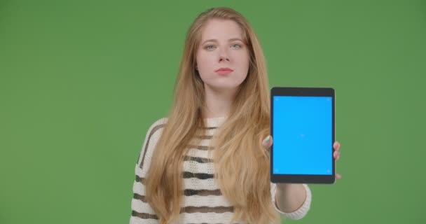 Närbild shoot av unga ganska kaukasiska kvinna använder tabletten och visar blå Chroma skärm till kamera med bakgrund isolerade på grön — Stockvideo