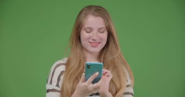 Closeup shoot of young pretty caucasian female using the phone and showing blue chroma key screen to camera holding it horizontally with isolated background — Stock Video