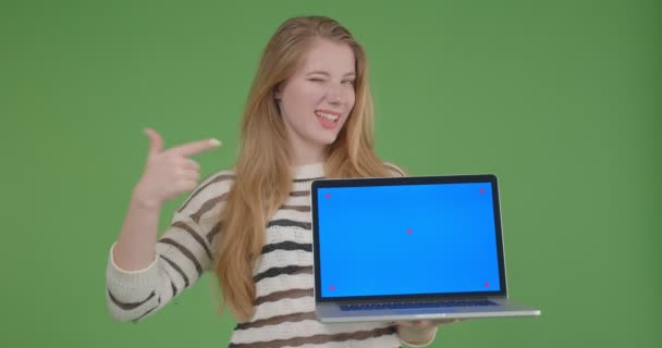 Nahaufnahme von jungen hübschen kaukasischen Frau hält den Laptop und zeigt Blue Screen in die Kamera lächeln fröhlich mit Hintergrund isoliert auf grün — Stockvideo