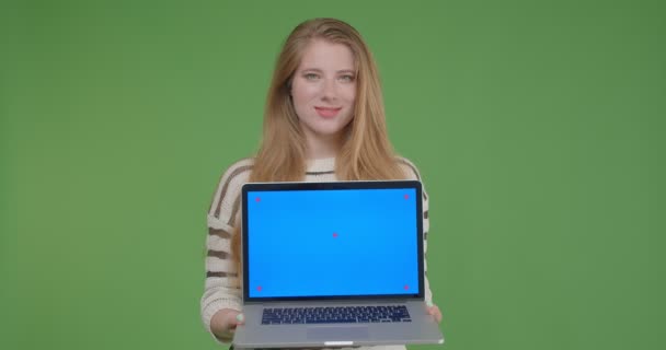 Κοντινό πλάνο του νεαρού όμορφο καυκάσιο θηλυκό κρατώντας το φορητό υπολογιστή και δείχνοντας μπλε οθόνη στην κάμερα με απομονωμένο φόντο — Αρχείο Βίντεο