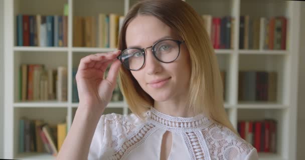 Primo piano ritratto di giovane studentessa caucasica in occhiali sorridente in posa allegra davanti alla telecamera nella biblioteca del college — Video Stock