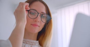 Gözlüklü genç beyaz beyaz iş kadınının dizüstü bilgisayarda çalışırken ki yakın çekim portresi beyaz bir odada ki kameraya neşeyle bakıyor