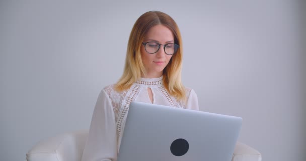 Retrato de close-up de jovem mulher de negócios muito caucasiana usando o laptop sorrindo alegremente olhando para a câmera dentro de casa em uma sala branca — Vídeo de Stock