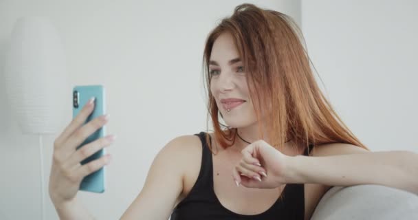 Close-up shoot van jonge sexy Kaukasische vrouw in zwarte Romper met een video-oproep op de telefoon praten vrolijk zittend op de Bank binnenshuis — Stockvideo