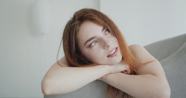 Крупный план съемки молодой сексуальной белой женщины в черном теле, лежащей на диване и радостно улыбающейся, глядя в камеру в помещении — стоковое видео