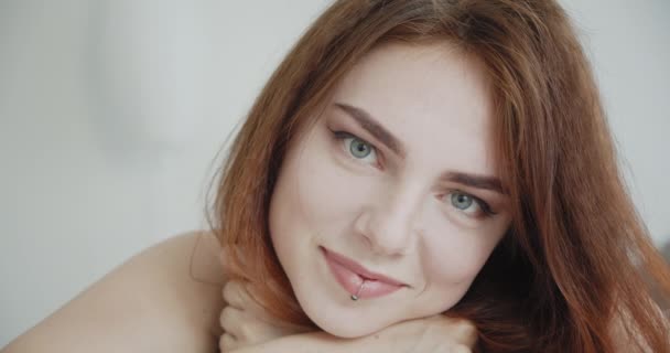 Крупный план съемки молодой сексуальной белой женщины, лежащей на диване и радостно улыбающейся, глядя на камеру в помещении — стоковое видео
