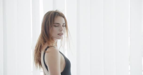 Съемки крупным планом молодой сексуальной белой женщины в черном купальнике, разворачивающейся, смотрящей в камеру и счастливо улыбающейся — стоковое видео