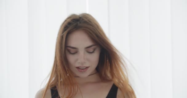 Nahaufnahme Shooting der jungen sexy kaukasischen Frau im schwarzen Body, die in die Kamera schaut und fröhlich lächelt, mit weißem Hintergrund — Stockvideo