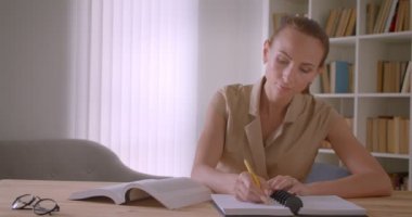 Kütüphanede ödev hazırlayan kitap ve kağıtlarla çalışan çekici öğretmen.