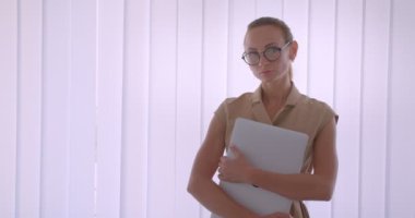 Dizüstü bilgisayarı kameraya tutan profesyonel kafkas yöneticisi pencerenin yanında dikkatle ve ciddi bir şekilde duruyor.