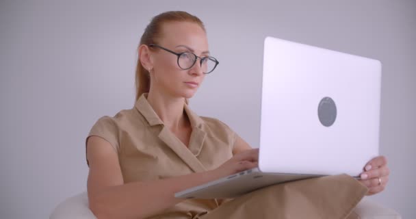 Elegante mujer de negocios caucásica sentada en sillón escribiendo en el ordenador portátil siendo considerado en la oficina blanca . — Vídeos de Stock