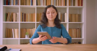 Tableti kullanan ve üniversite kütüphanesinde kameraya yeşil ekran gösteren genç ve beyaz beyaz kız öğrencinin yakın çekim portresi kapalı