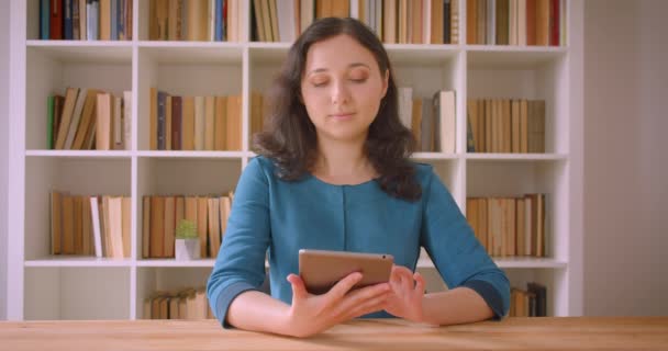 Крупним планом портрет молодої досить кавказької студентки, що використовує планшет і показує зелений екран хрому для камери в бібліотеці коледжу в приміщенні — стокове відео