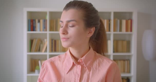 Üniversite kütüphanesinde mutlu bir şekilde gülümseyen kameraya bakan genç çekici kız öğrencinin yakın çekim portresi — Stok video