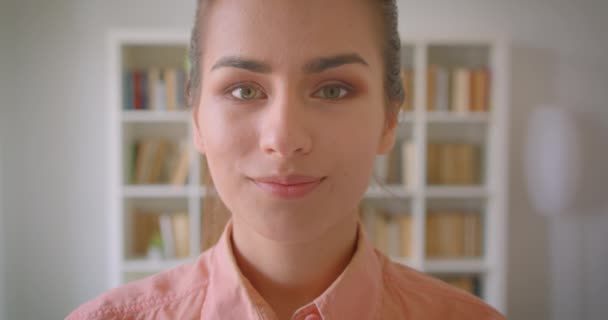 Närbild porträtt av unga ganska kvinnlig student tittar på kamera leende glatt i kollegiet biblioteket — Stockvideo