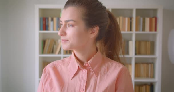 Üniversite kütüphanesinde mutlu bir şekilde gülümseyen kameraya bakan genç sevimli kız öğrencinin closeup portresi — Stok video
