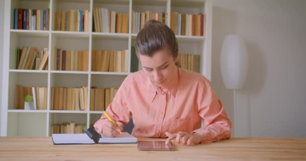 Retrato de cerca de una joven estudiante atractiva que estudia y usa la tableta en la biblioteca de la universidad — Vídeo de stock