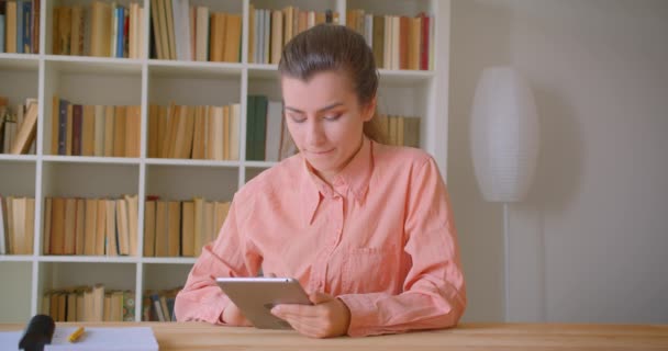 Nahaufnahme Porträt einer jungen attraktiven Studentin beim Surfen auf dem Tablet in der Hochschulbibliothek — Stockvideo