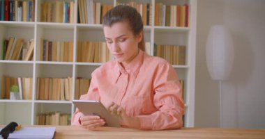 Tableti kullanan ve üniversite kütüphanesinde kameraya yeşil ekran gösteren genç çekici kız öğrencinin closeup portresi