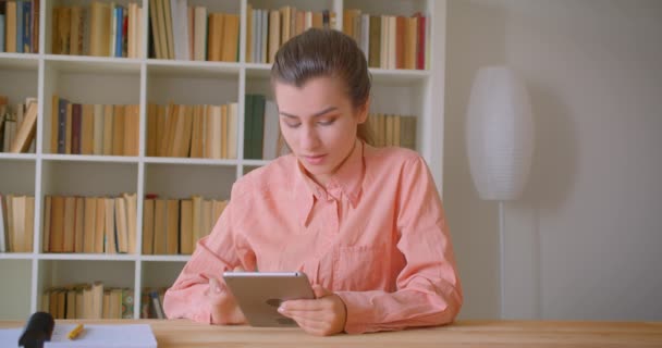 Retrato de close-up de jovem atraente estudante mensagens de texto no tablet na biblioteca da faculdade — Vídeo de Stock