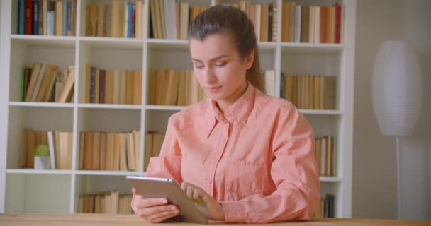 Zbliżenie Portret młodej atrakcyjnej studentki za pomocą tabletu i pokazując zielony ekran klucza chrominancji do kamery w bibliotece kolegium — Wideo stockowe