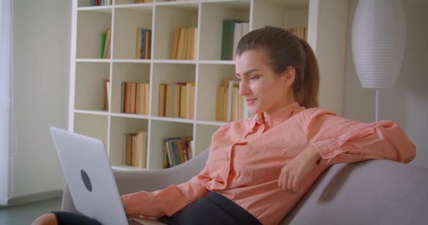 Крупный план портрета молодой привлекательной деловой женщины, работающей на ноутбуке, смотрящей в камеру и радостно улыбающейся сидящей дома на диване — стоковое видео