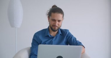 Rahat ve hafif ofis içinde koltukta oturan dizüstü bilgisayar ile çalışan at kuyruğu ile Progressive freelancer kameraya gülümsüyor.