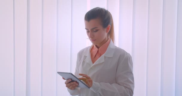 Retrato de primer plano de la joven atractiva doctora caucásica sosteniendo una tableta y mostrando la pantalla verde a la cámara de pie en el interior — Vídeo de stock