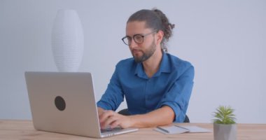 Hafif ofiste dizüstü bilgisayarda yazarak at kuyruğu ve gözlük ile Modern freelancer kameraya sevinçle gülümsüyor.