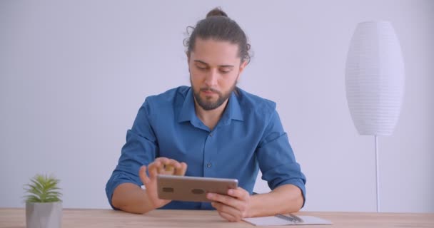 Modern businessman with ponytail working with tablet shows green chroma screen with app to camera in white office. — Stock Video