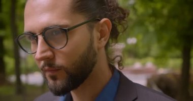 At kuyruğu ile resmi takım elbise yakışıklı hipster adam yakın çekim parkta kamera içine baştan çıkarıcı gülümseyerek.