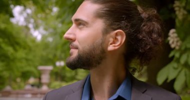 At kuyruğu ile resmi takım elbise yakışıklı hipster adam kameraya döner ve parkta içine sevinçle gülümsüyor.