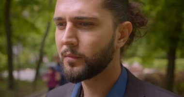 Parkta kafası karışan at kuyruğu ile resmi takım elbiseli yakışıklı hipster adamın yakın çekim çekimi kameraya kadar izlerken.